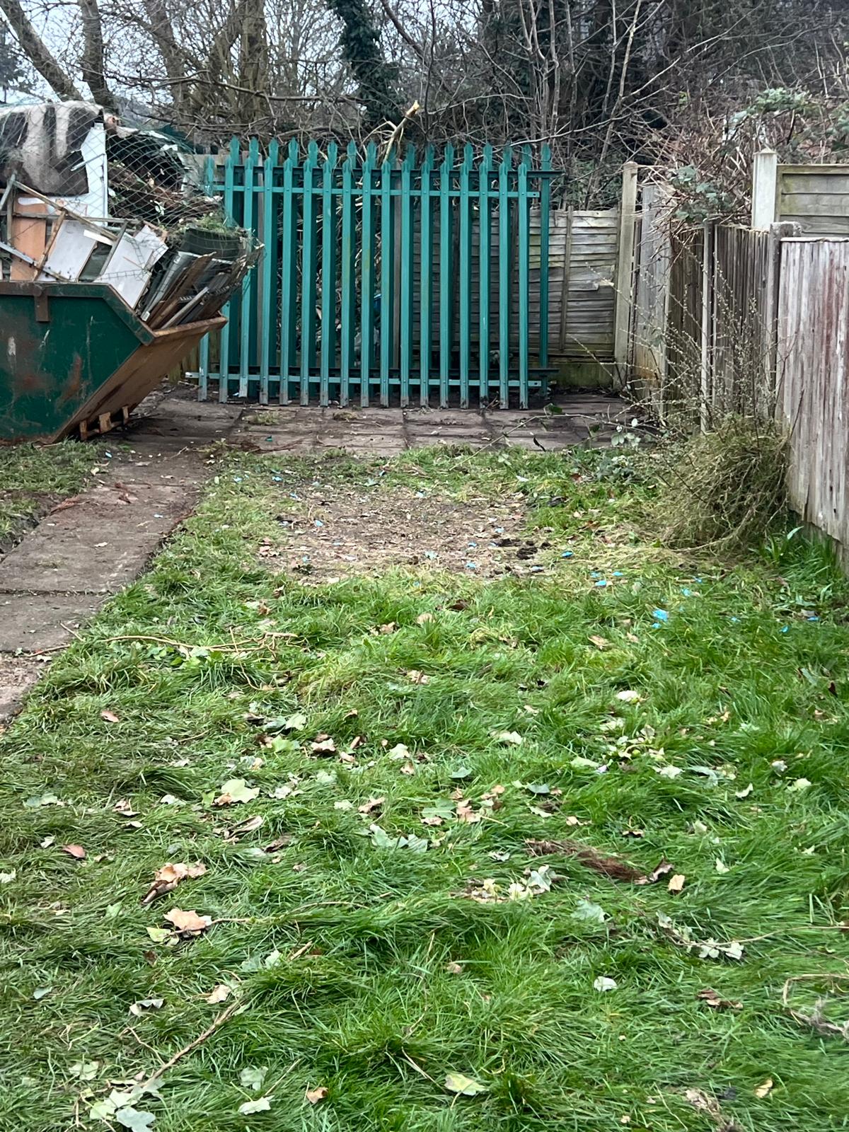 Garden with green palisade fencing and skip during clearance work