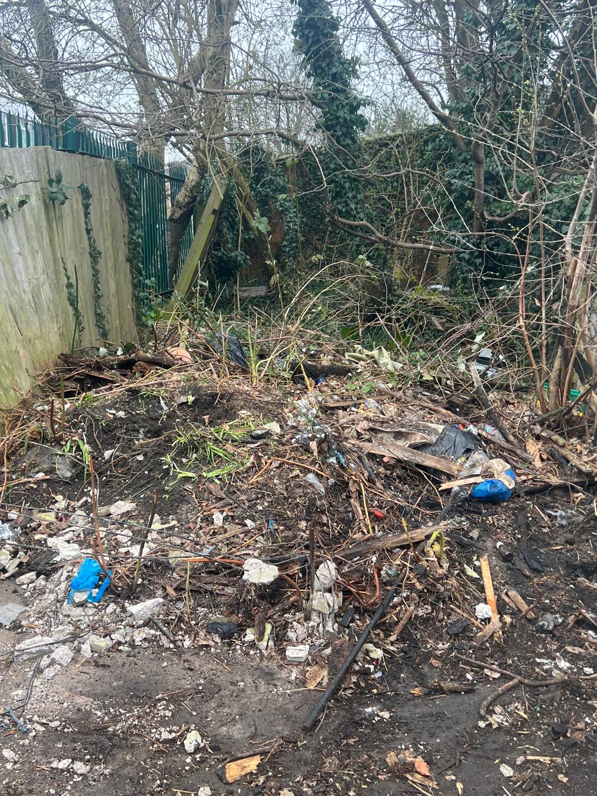 Overgrown garden area cleared with waste pile and old fencing