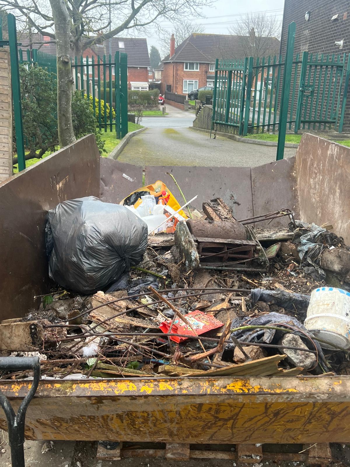 Skip filled with garden debris and waste bags on residential street