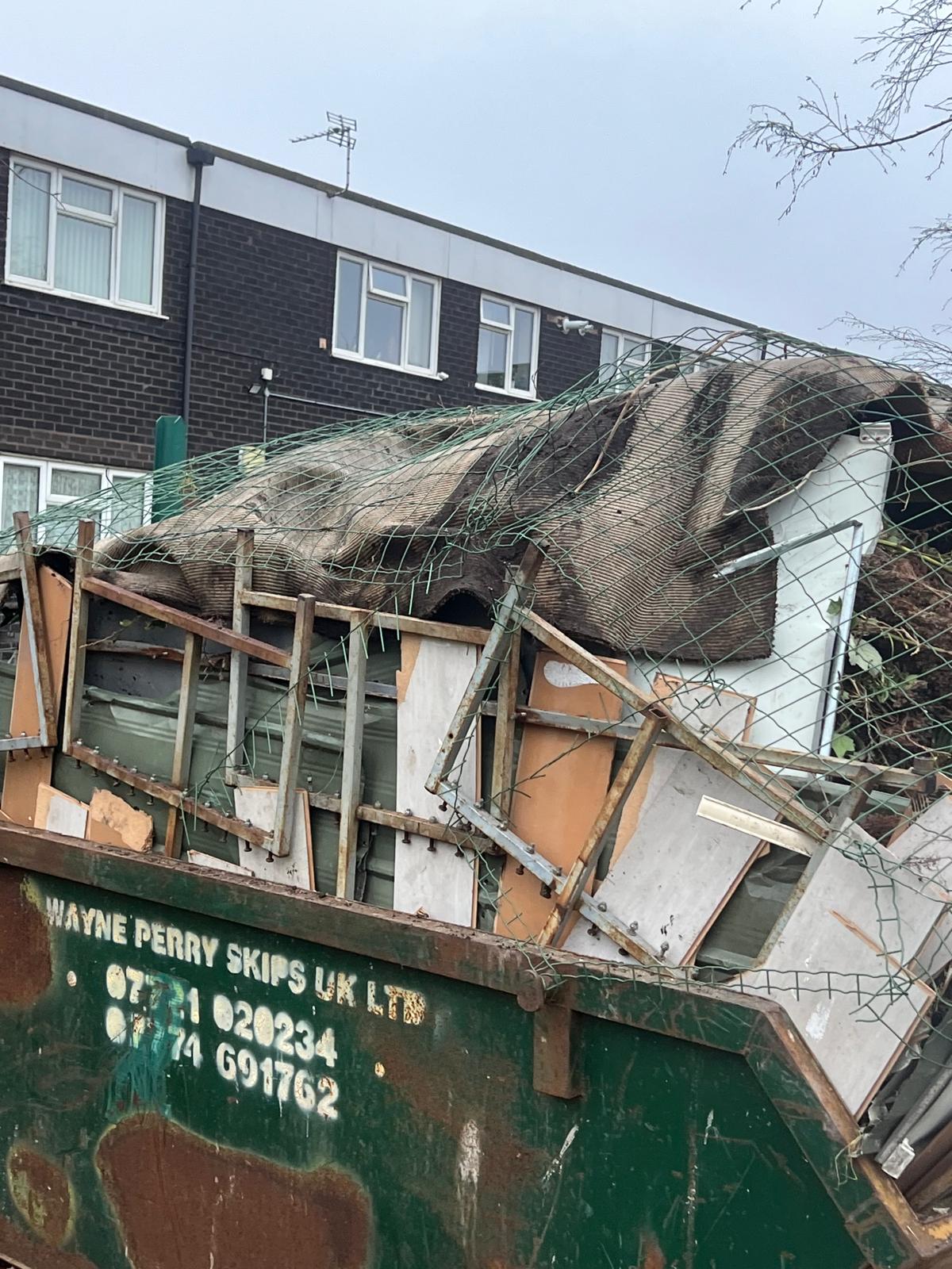 Full skip loaded with garden waste and old fencing after clearance job